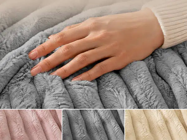 A close-up of a person's hand resting on a plush, ribbed gray blanket. The image includes three smaller color swatch panels along the bottom showing the fabric texture in pink, gray, and beige.