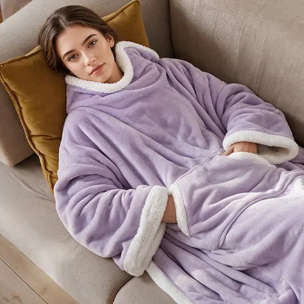 A woman reclining on a beige couch wearing a lavender purple wearable electric heated blanket.